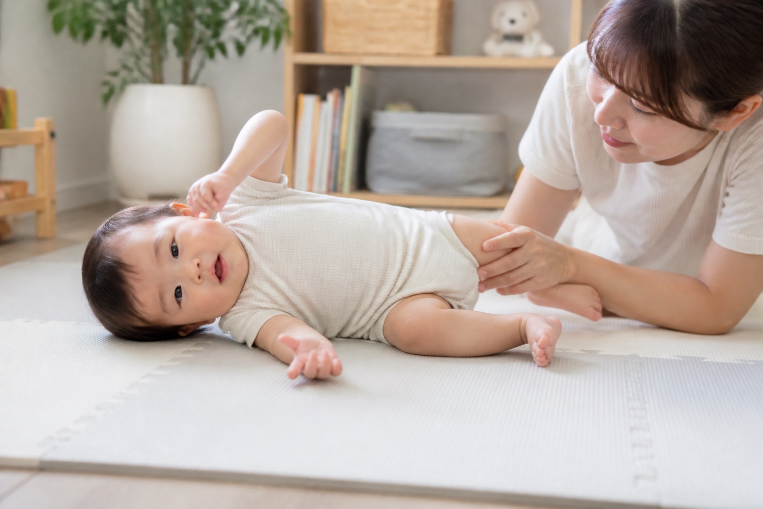 床のマットで横向きへ寝返ろうとする赤ちゃんを支える保護者