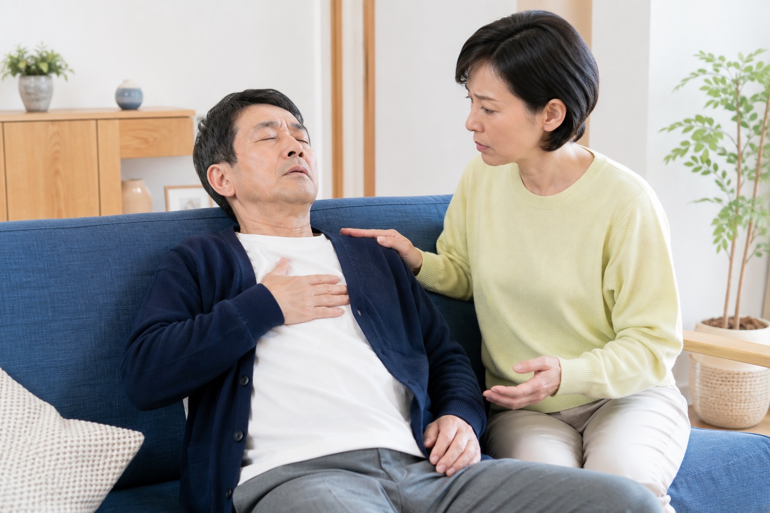 急な胸の苦しさで休む男性をそばで見守り受診を考える家族