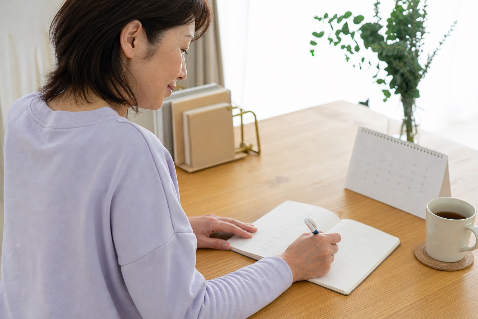 月経や下腹部痛の時刻をカレンダーとノートへ記録する女性