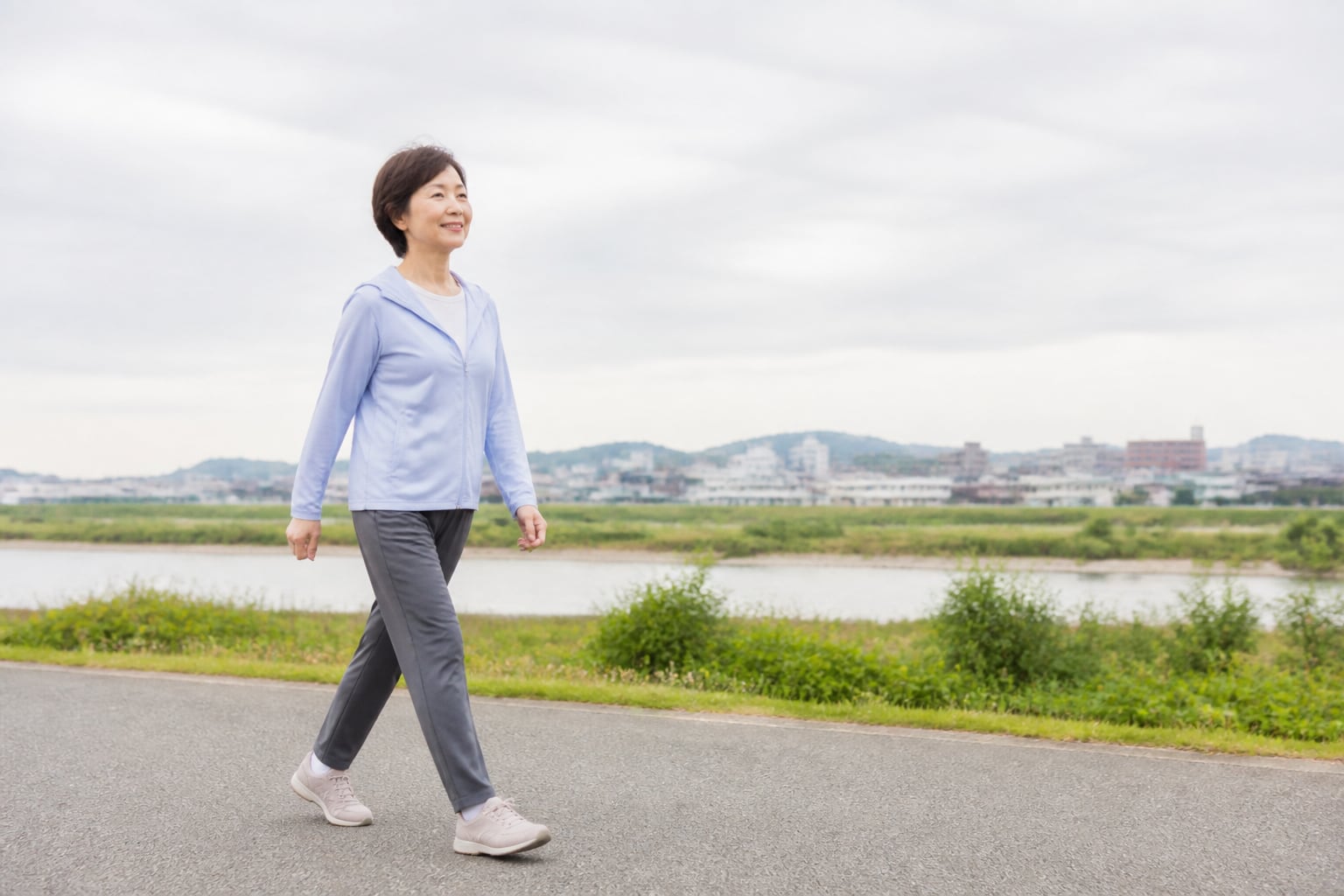 川沿いの平らな道を無理のない歩幅で歩く女性
