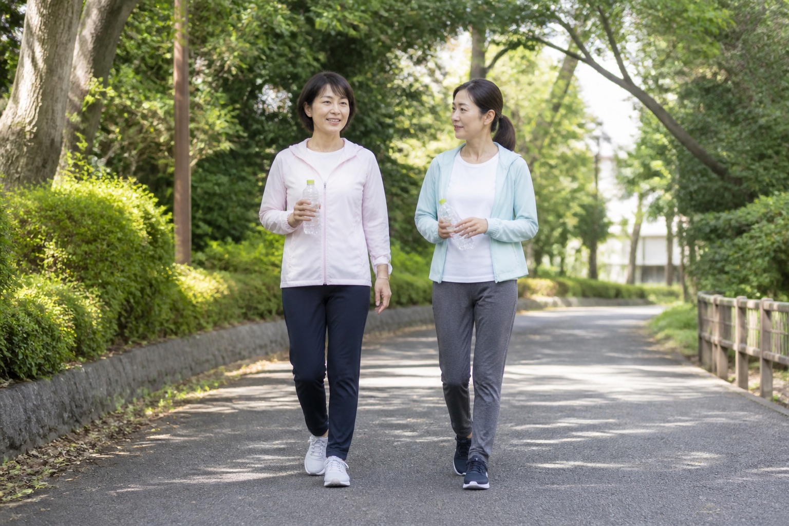 朝の公園で水分を持って無理なく歩く50代女性二人