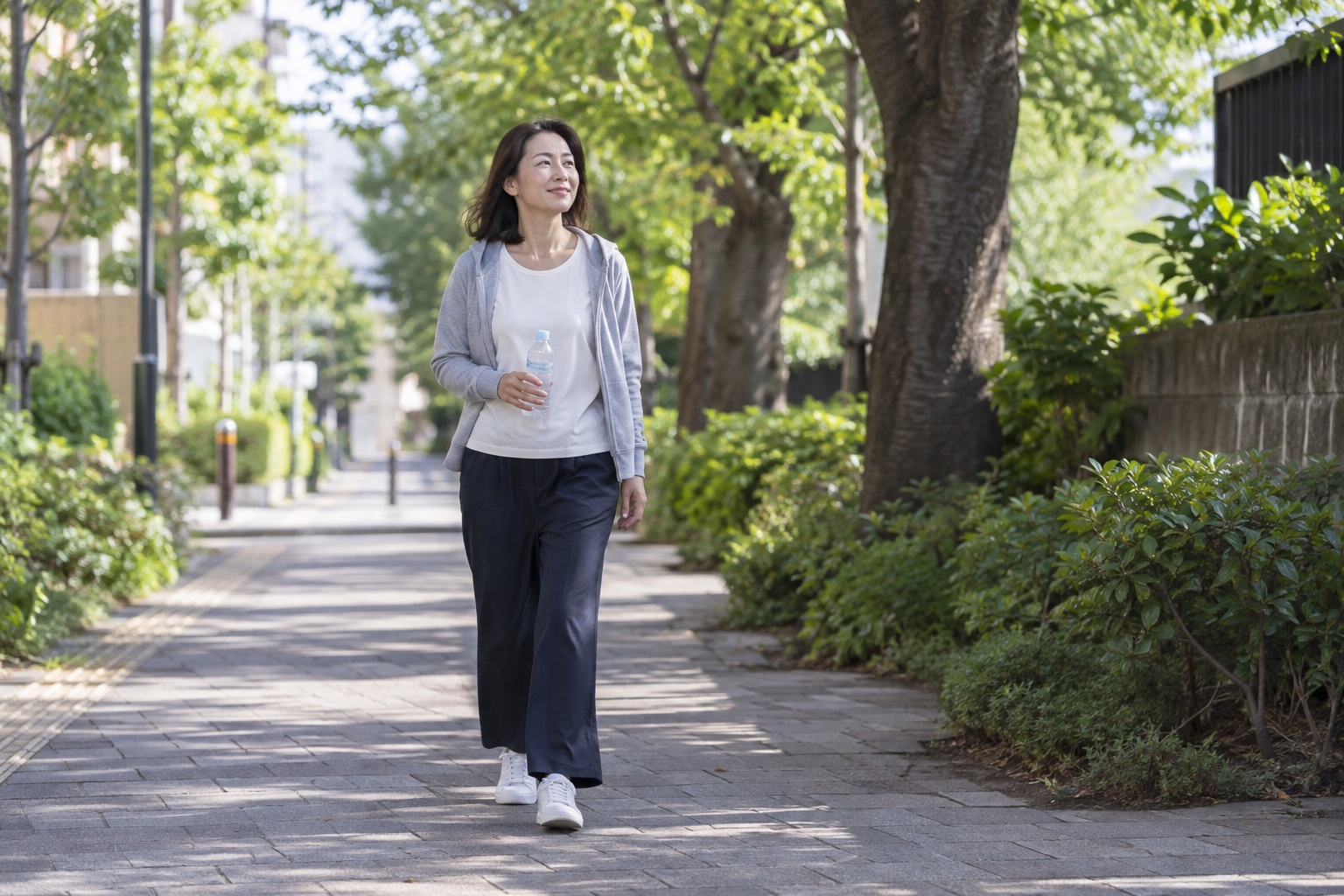 体調を確認しながら水を持って緑道を歩く女性