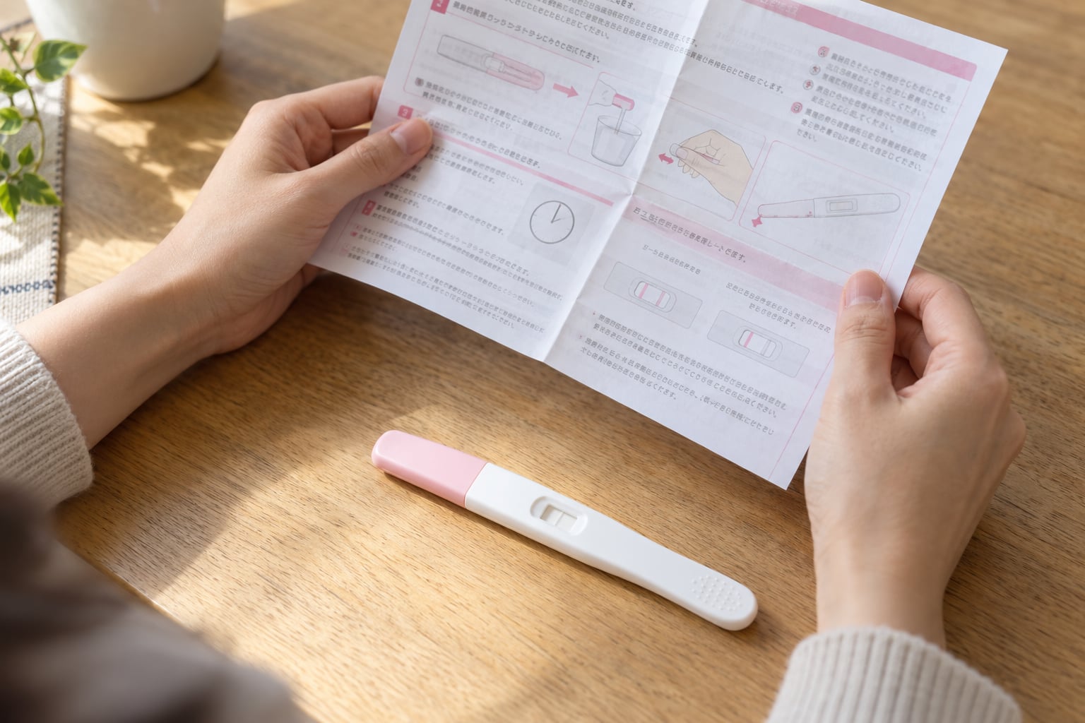 妊娠検査薬を机に置き添付説明書を両手で確かめる手元