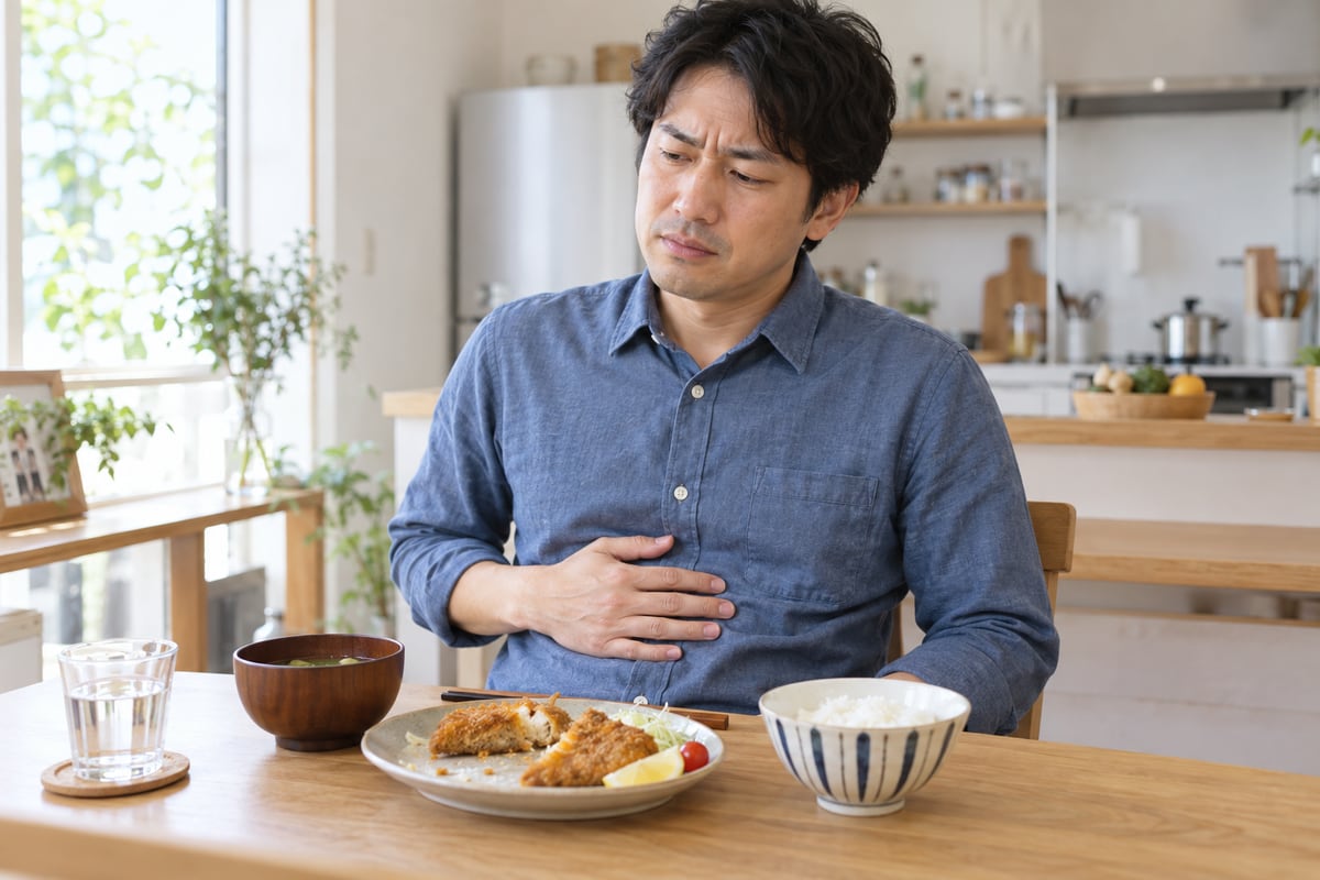 揚げ物の昼食後に椅子へ座り、みぞおちに手を添える青いシャツの男性